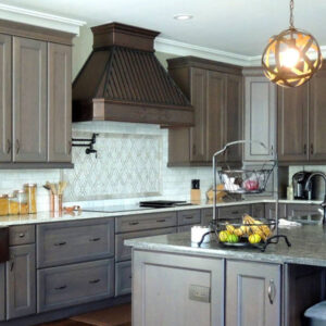 A stylish range hood in a well - designed kitchen with gray cabinetry and a marble - topped island.