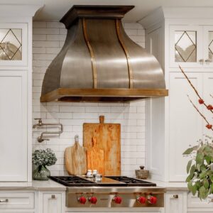 A stunning stainless - steel range hood with brass accents in a bright white kitchen.